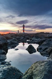 Volcanic Rock Prints: El Toston lighthouse reflected in the sea at sunrise
