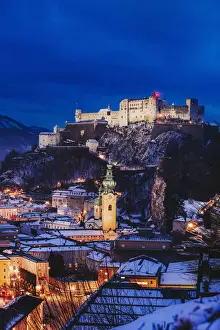Elevated view of Salzburg city by night on a winter evening with the roofs covered