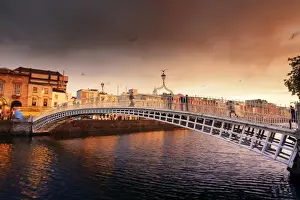 Europe, Dublin, Ireland, people crossing Halfpenny bridge on the Liffey river at sunset