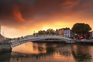 Europe, Dublin, Ireland, people crossing Halfpenny bridge on the Liffey river at sunset