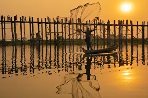 Pedestrian Bridge Prints: Fisherman throwing fishing net at Taungthaman Lake against U Bein bridge at sunset