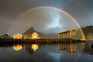 Reine Prints: Fishermen cabins under a dramatic cloudy sky with rainbow at dawn