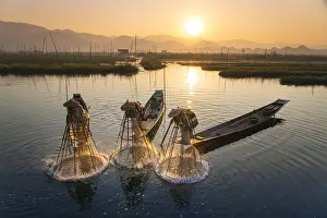 Three fishermen catching fish from boats using traditional conical nets at sunrise