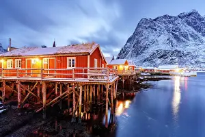 Cloudscape Prints: Fishermen huts framed by snowcapped mountains reflected in the icy sea at dusk