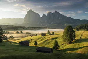 A foggy sunrise, Alpe di Siusi (Seiser Alm), with the Sassolungo and Sassopiatto and wooden cabins. Dolomites, Italy