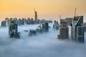 Foggy sunrise with Dubai Marins skyscrapers towering over the low clouds, Dubai