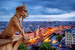 Paris Prints: Gargoyle on Notre Dame Cathedral at night overlooking the city of Paris, France