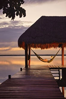 Quiet Gallery: Girl with hat in a hammock looking at Bacalar lagoon at sunrise from a pier, Quintana Roo