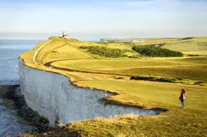 High Gallery: Girl looking at the Seven Sisters Cliffs in the early morning with Belle Tout lighthouse