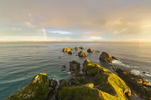Ahuriri Flat Gallery: Golden light on The Nuggets islands and rainbow in the sky at Nugget Point. Ahuriri Flat