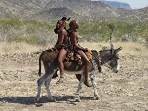 Traditional Attire Gallery: Two happy Himba girls ride a donkey to market