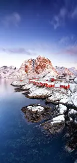 Lofoten Prints: High angle view of red fishermen huts on cliffs covered with snow at dawn