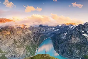 High Up Prints: Hiker man with backpack admiring sunset over lake Limmernsee from top of rocks
