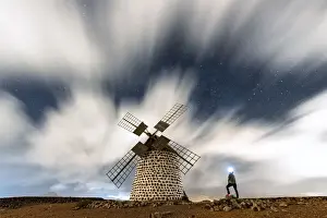 Mill Prints: Hiker man with head torch admiring clouds in the starry sky over the windmill, La Oliva