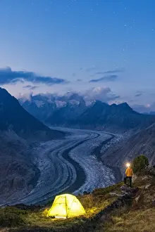 Hiker man with head torch light admiring Aletsch Glacier standing beside the tent