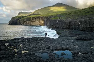 Images Dated 15th November 2022: A hiker standing along the coast of the village of Eiði at sunset. Island of Eysturoy