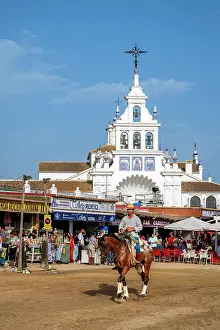 Rocio Prints: Horseman riding in a street with Ermita de la Virgen del Rocio in the background