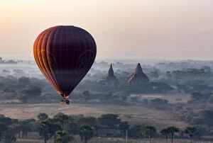 A hot air balloon flies over a temple at sunrise on a misty morning, Bagan, Myanmar