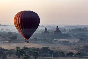 A hot air balloon flies over a temple at sunrise on a misty morning, Bagan, Myanmar A hot air balloon flies over a temple at sunrise on a misty morning, Bagan, Myanmar