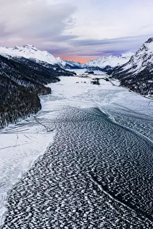 Frozen Water Prints: Ice and snow covering Lake Silvaplana during the winter sunrise, aerial view, Maloja