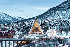 Winding Road Prints: Illuminated Arctic Cathedral and houses covered with snow at dusk, Tromso, Norway