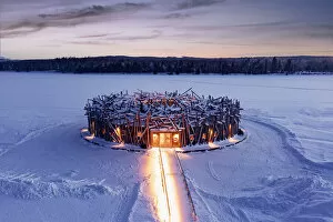 Illuminated circular building of the floating Arctic Bath Hotel and walkway covered with snow at dusk, Harads, Lapland
