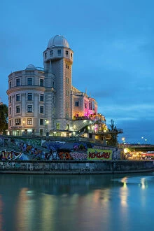 Illuminated Urania Observatory by Danube river canal at twilight, Innere Stadt, Vienna, Austria