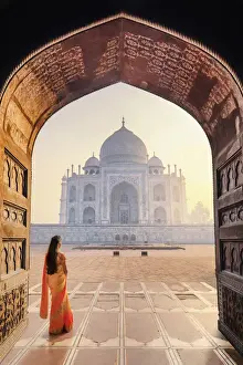 India, a beautiful woman in a red and yellow sari in front of the Taj Mahal at sunrise