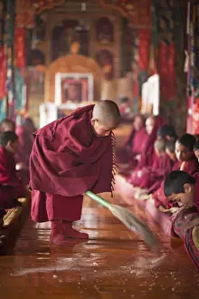 Gelugpa Prints: India, Ladakh, Thiksey. Young novice monk sweeping up the tsampa crumbs at morning prayers or puja