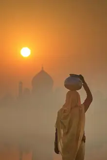 India, water carrying a water pot on a foggy morning with the sun rising on the Taj Mahal