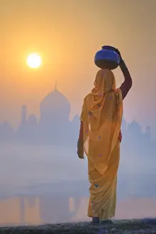 India, water carrying a water pot on a foggy morning with the sun rising on the Taj Mahal