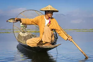 Intha fisherman with a traditional conical fishing net showing fish against clear sky