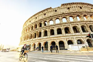 Colosseum Prints: Italy, Rome, a woman riding a bike Colosseum and Roman Forum at sunrise