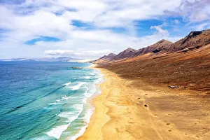 Volcanic Landscape Prints: jeep traveling on empty Cofete Beach washed by ocean waves, Jandia, Fuerteventura