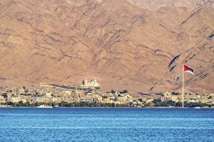 Jordan, Aqaba Governorate, Aqaba. Jordanian flag and buildings in front of mountains