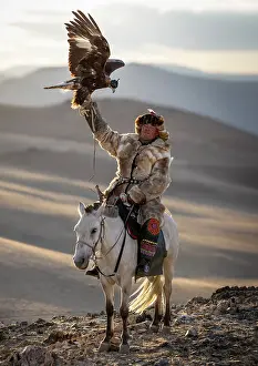Mongolia Prints: Kazakh Eagle Hunter on horseback wearing traditional fur clothing and posing with his trained golden eagle