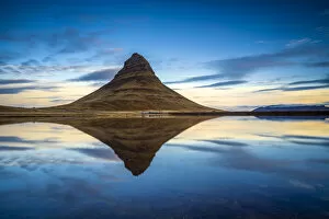 Kirkjufell mountain reflecting in still water against blue sky during sunset