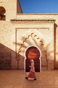 Tall Building Prints: Lady in traditional dress in front of door at Koutoubia Mosque, Marrakech, Morocco