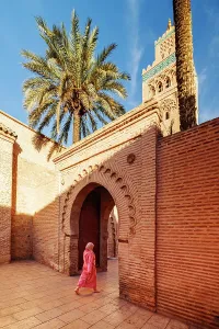 Marrakech Prints: Lady in traditional dress walking through doorway at Koutoubia Mosque, Marrakech, Morocco
