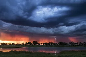 Images Dated 17th June 2020: Lightning shoots from a summer thunderstorm as the sun sets behind it, Okavango Delta