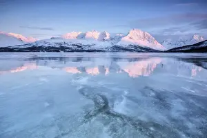 The last lights of dusk coloring the snowy Lyngen alps reflecting in the half frozen