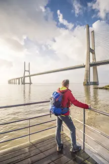 Suspension Bridge Prints: Lisbon, Portugal. Man with backback watching the Vasco Da Gama bridge at sunrise