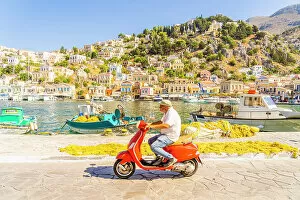 Dodecanese Islands Gallery: A local man riding a red Vespa in the colourful harbour in Symi, Dodecanese Islands, Greece