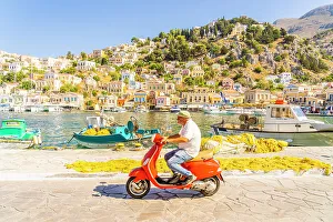 Aegean Prints: A local man riding a red Vespa in the colourful harbour in Symi