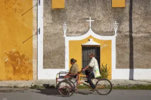 Locals on a tricycle passing by the front facade of a colonial house in Izamal, Yucatan, Mexico
