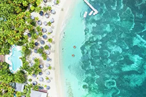Drone Collection: Luxury resort with swimming pool and beach umbrellas on palm fringed beach from above, Antigua