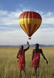 Two Maasai warriors watch a hot air balloon flight over Masai Mara