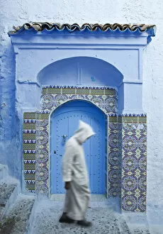 Images Dated 21st December 2020: Man in Burnoose walking past blue doorway, Chefchaouen, Morocco