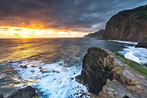 Man on cliffs looking at waves at dawn, Miradouro Do Guindaste viewpoint, Madeira island