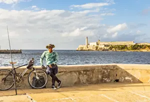 Habana Prints: A man with fishing equipment on the Malacon with Castillo De Los Tres Reyes Del Morro